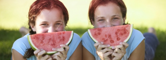 Imagem de duas jovens com uma fatia de melancia em frente do rosto. Esta imagem ilustra como estas sugestões para te sentires bem te ajudarão a fazer aquilo que mais gostas, durante a menstruação. 