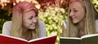 Imagem de duas jovens a ler um livro. A imagem ilustra os vários mitos que estão associados à menstruação.